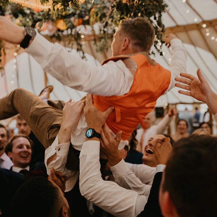 Groomsmen lift up the groom during the wedding reception