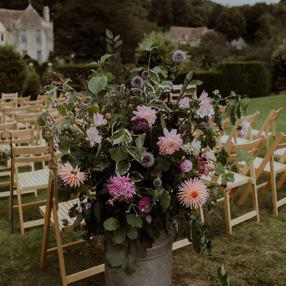 Pink and purple wedding flowers in vintage milk churns including dahlias and thistle 