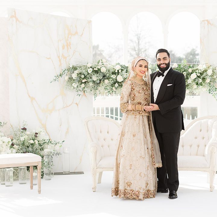 Bride & groom are surrounded by fresh white floral bouquets complete with green foliage in front of window 