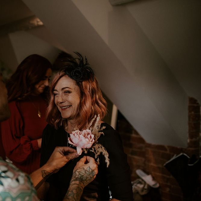 Groom puts floral buttonhole on mother on the morning of his wedding day