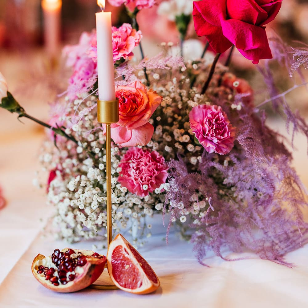 Bright pink wedding flowers for modern tablescape finished with pastel candles in gold candle holders and dried fruit decor 