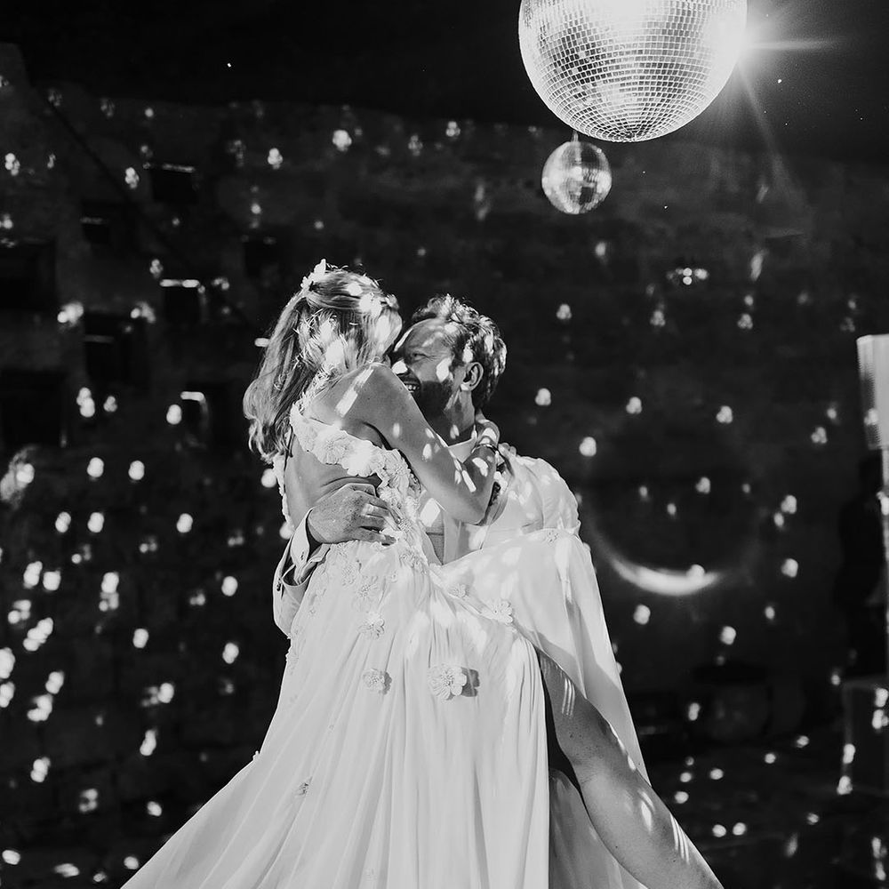 Groom lifts the bride for their first dance together with the disco ball shining 