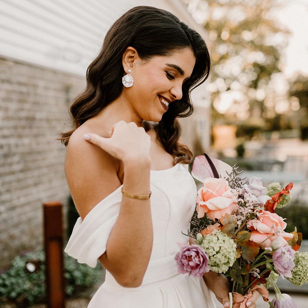 Bride with pearl earrings holding a pretty colourful wedding bouquet with pretty Hollywood waves