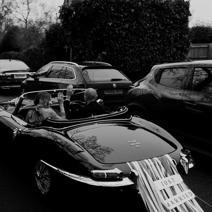 Bride and groom in classic convertible wedding car with streamers and just married sign