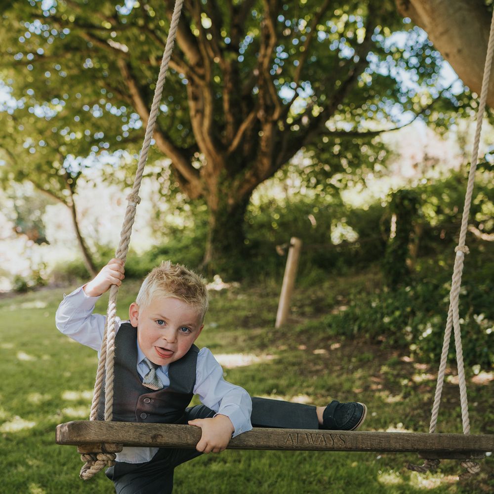 Page boy climbs onto wooden swing outdoors at Watermouth Cove