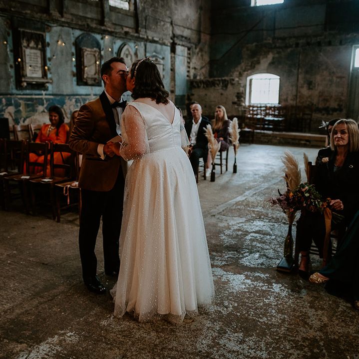 Bride and Groom share a kiss at alter in London venue decorated with fairy lights