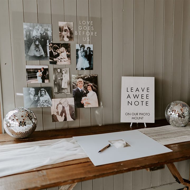 Wedding guest on wooden table with white table runner and disco balls with photos of family weddings and a black and white sign with Scottish dialect