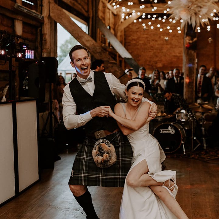 Groom in waistcoat and kilt shares the first dance with the bride in a sparkly wedding dress with a sleek updo hairstyle 