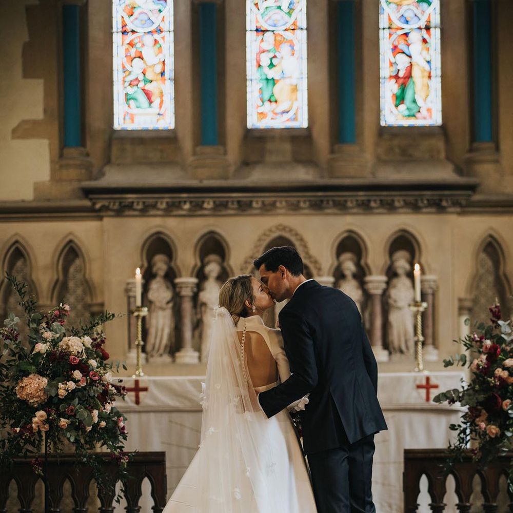 Bride in illusion back button detail wedding dress kissing the groom in black tie for their church wedding ceremony