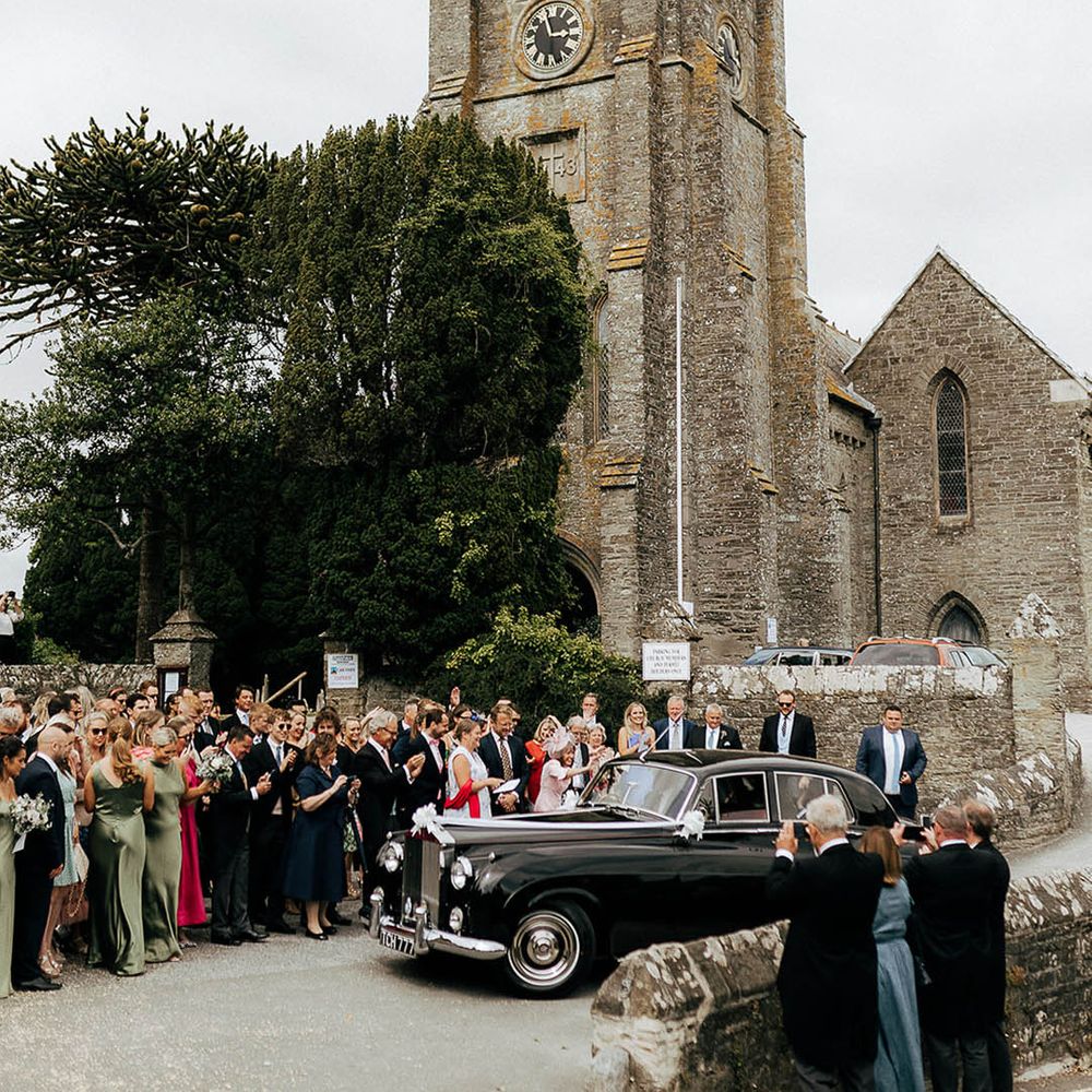 Vintage black wedding car beside wedding guests for church ceremony 