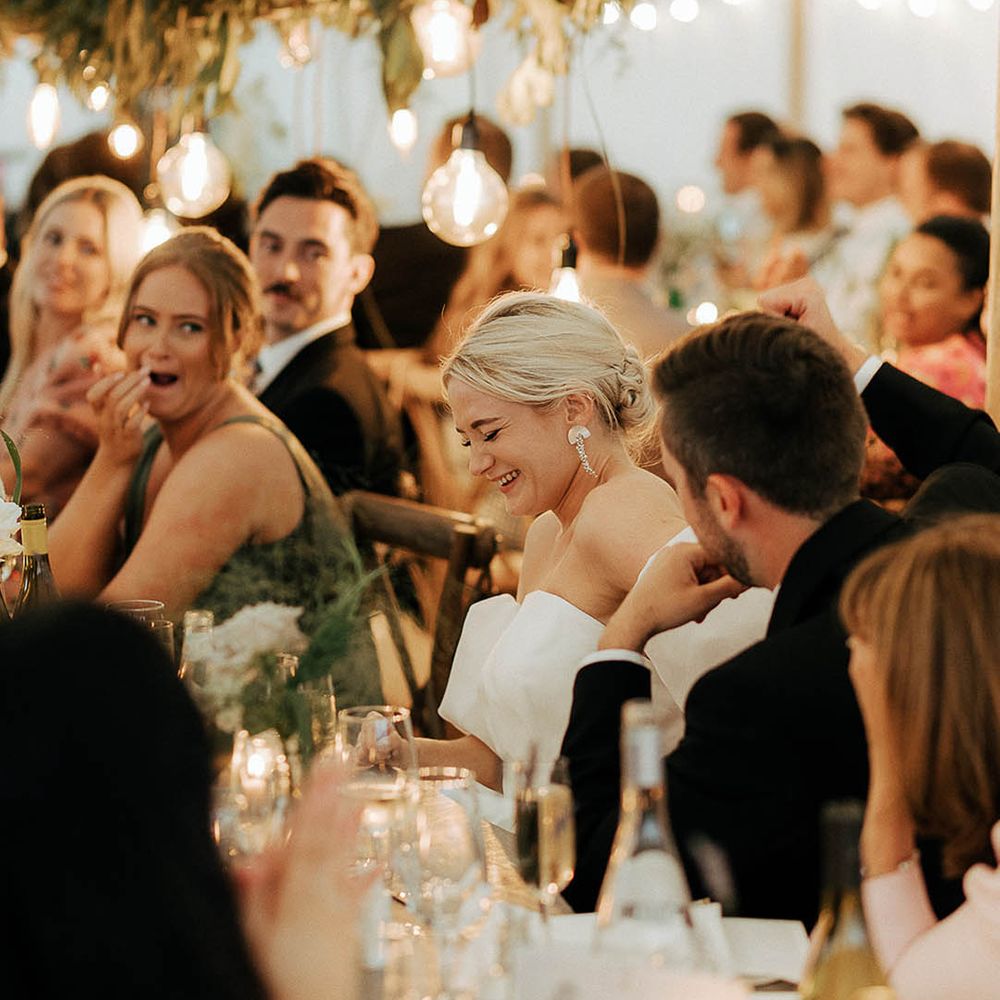 Bride laughs during wedding reception in marquee complete with green foliage installations 