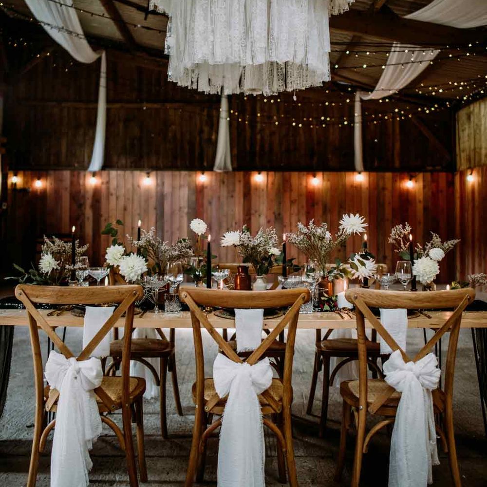 Rustic luxury wedding tablescape with white drapery over the chandelier, white tulle ribbons on the backs of the chairs, fairy lights and white floral centrepieces - wedding budget spreadsheet 