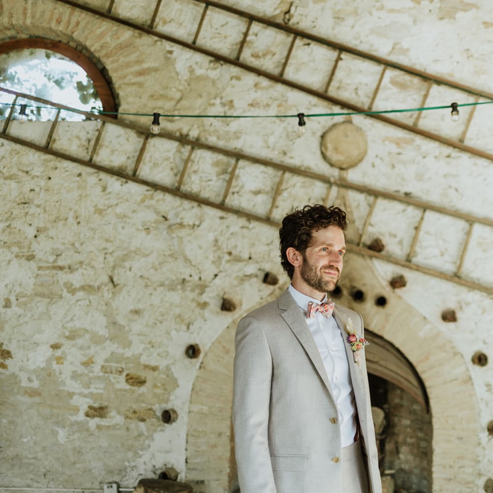 Groom in greige suit and colourful bow tie at rustic wedding venue in Italy