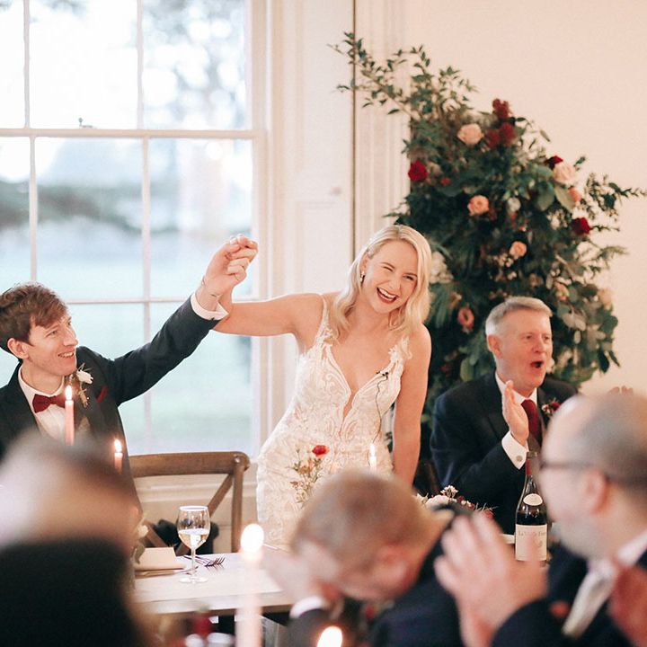Bride and groom sit at their wedding breakfast in front of festive flower columns 