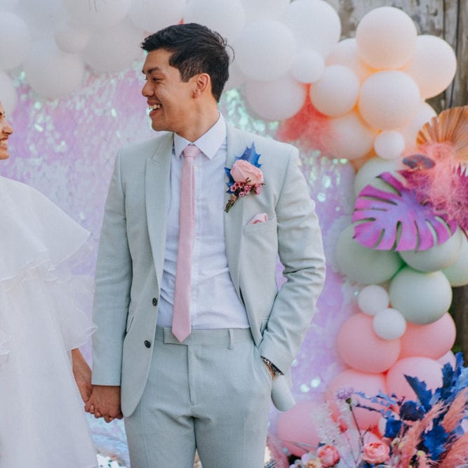 Bride in short wedding dress and boots and groom in pale green suit holding hands 