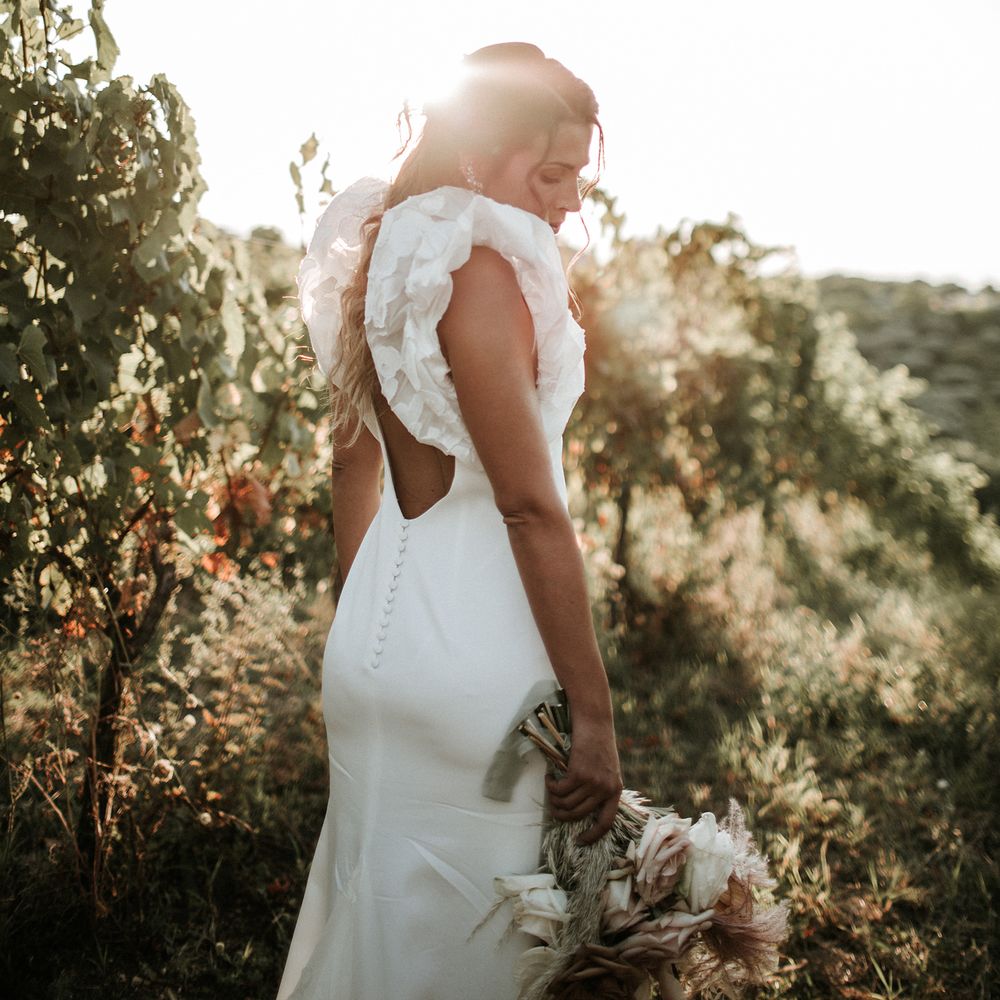 Bride in a Rime Arodaky wedding dress with low back detail, buttons and ruffle sleeves standing in a field 
