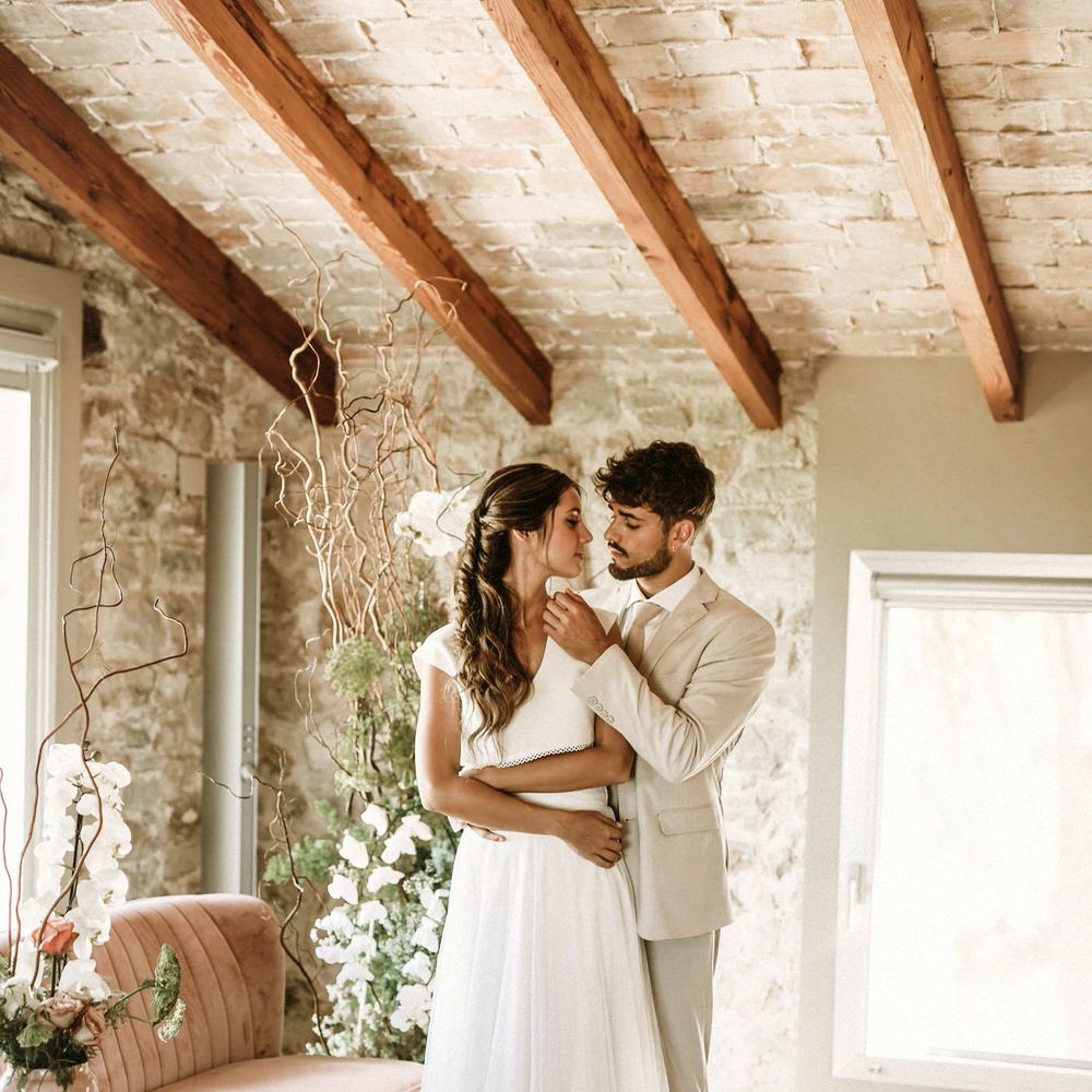 Beaded groom in a beige suit caressing his brides face standing on wicker rugs 