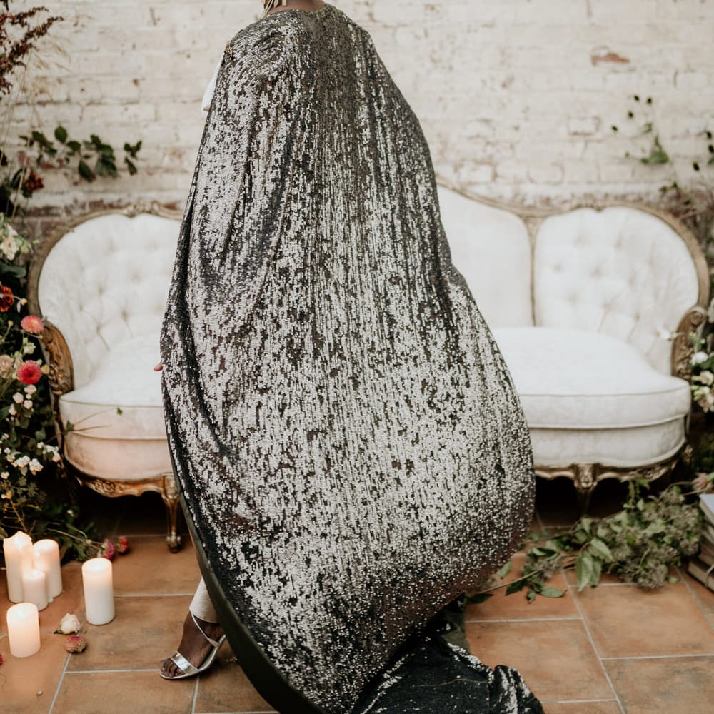 Bride with alopecia in a black and silver shimmers bridal cape statement gold earrings and bridal cown 