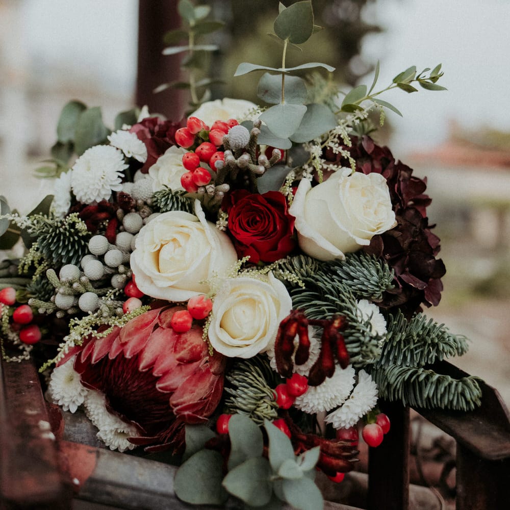 A bouquet of red and white roses, eucalyptus and pine leaves, berries and seasonal blooms
