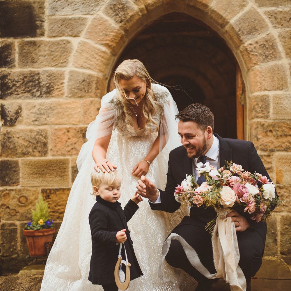 Groom in a navy suit bending down talking to a little wedding guest 