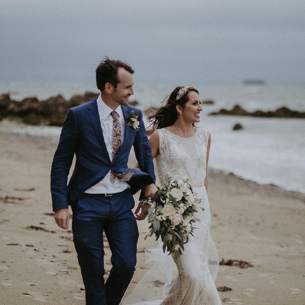 Bride & groom walk together along the beach on their wedding day