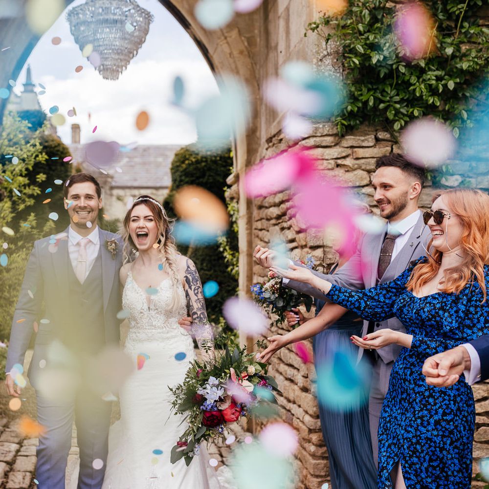 Bride & groom walk through wedding party throwing colourful confetti on their wedding day