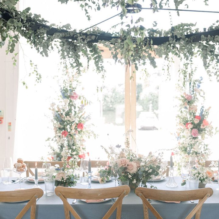 Intimate wedding reception at The White Barn with hanging foliage installation, blue table cloth, pastel centrepiece flowers, and taper candles 