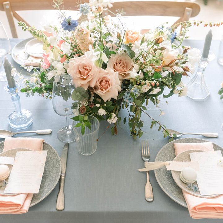 Pastel pink and peach wedding reception table decor with blue tablecloth, peach linen, and floral centrepieces 