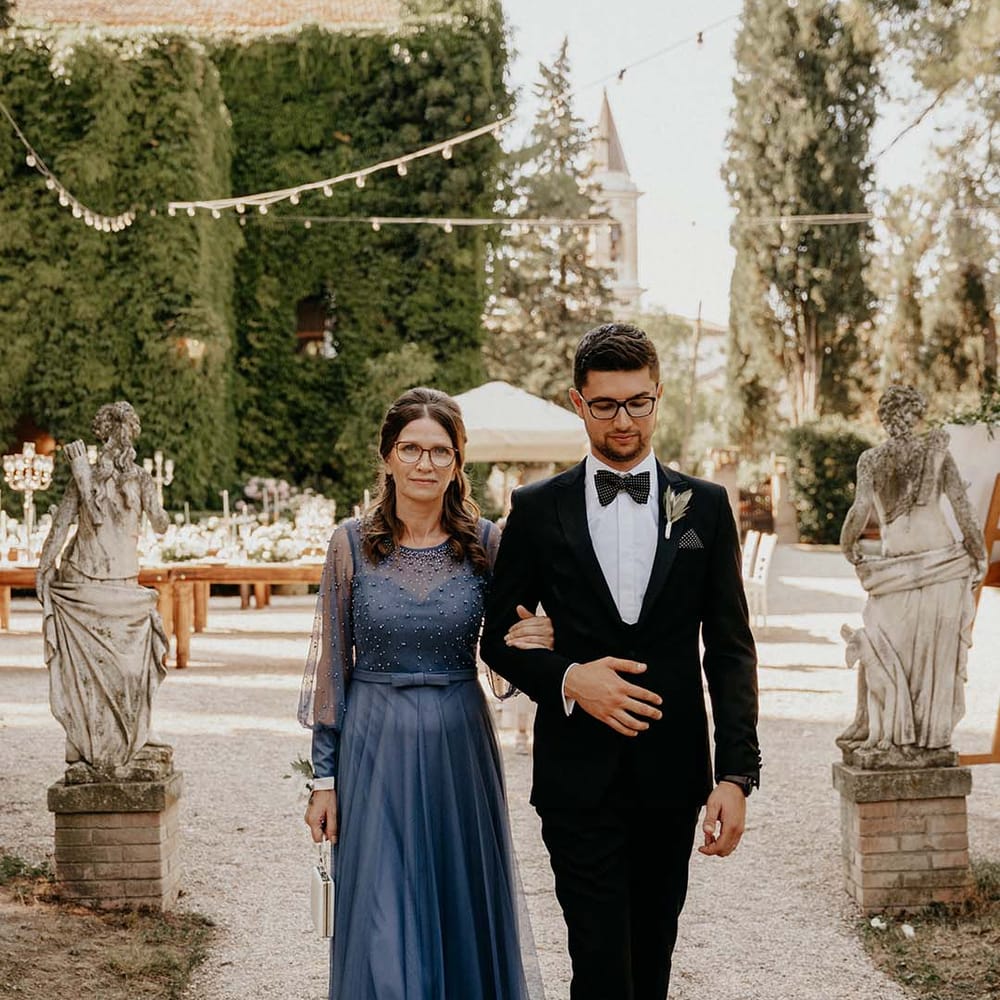 Groom walks down in the aisle with his mother who wears long deep blue gown | Royal Studio
