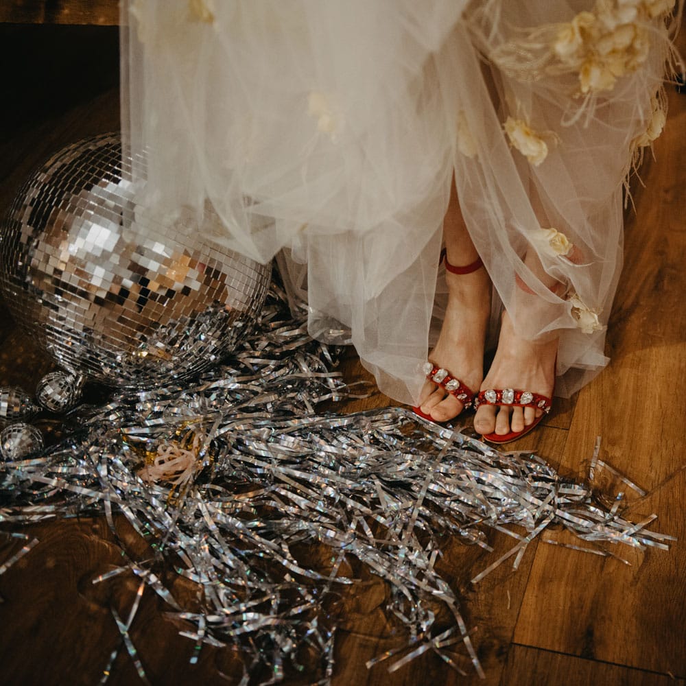 Bride in tulle wedding dress lifts up skirt to show red heeled sandals at rustic wedding in Lancashire