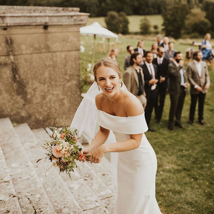 Bride wears off the shoulder bridal gown and holds floral bouquet