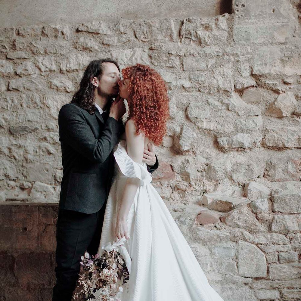 Groom in a wool suit kissing his bride in a princess wedding dress with red curly hair 