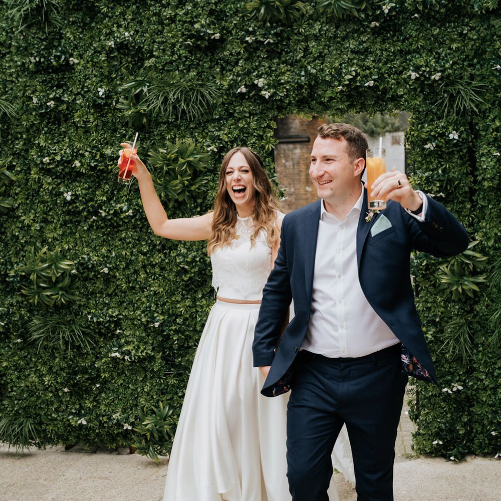 Bride and groom enter their reception holding alcoholic beverages ready to celebrate