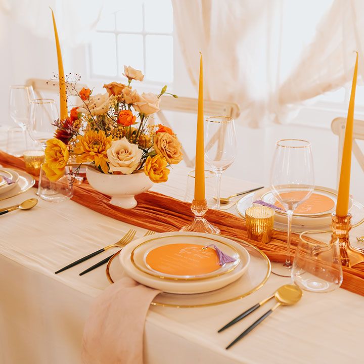 golden wedding table decor with orange table runner, yellow taper candles and flower arrangements 