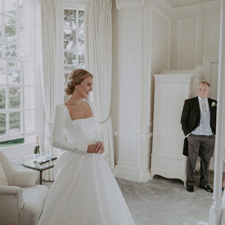 Bride in long white wedding dress with square neck, full skirt and pearl necklace 