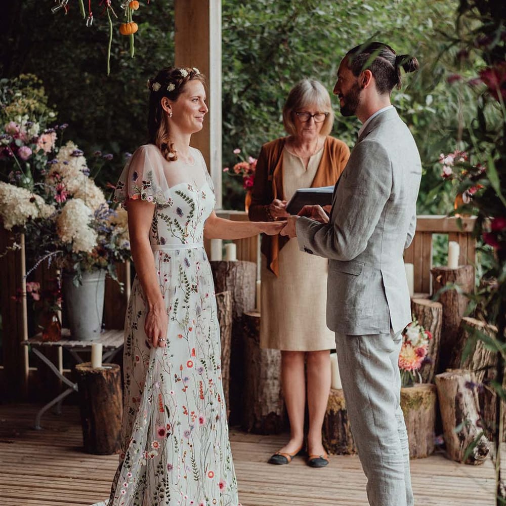 Bride in floral embroidery wedding dress and groom in grey suit at the altar with hanging mini pumpkin decoration and flower decorations for botanical wedding 