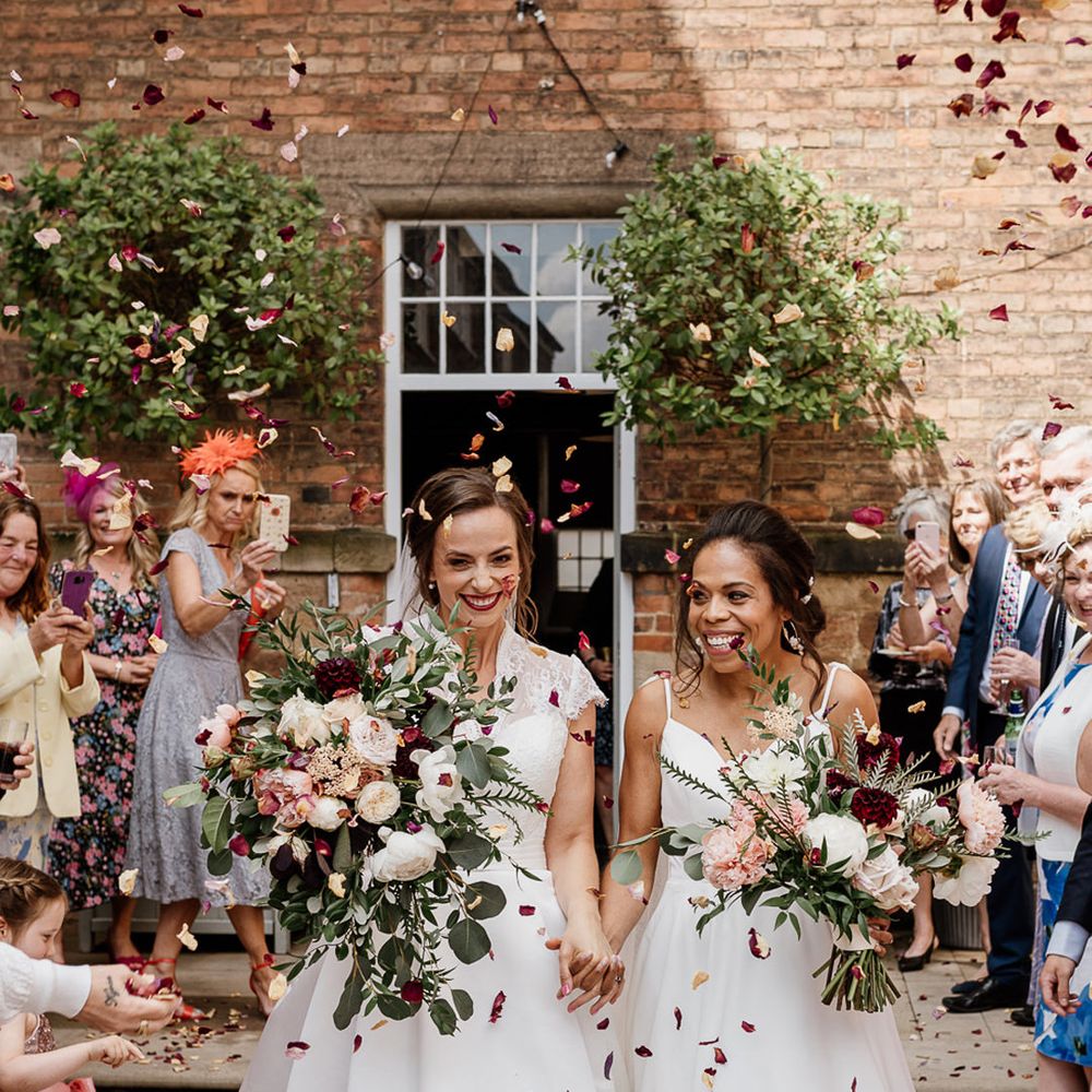 Confetti Moment at The West Mill with two brides in princes wedding dresses holding giant white, burgundy and green wedding bouquets 