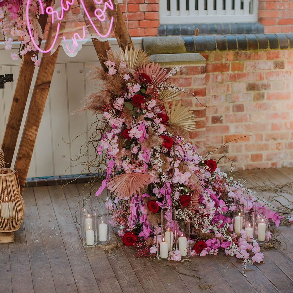 Wedding flower arrangement with pink cherry blossom, dried palm leaves, pampas grass and roses surrounded by pillar candles 