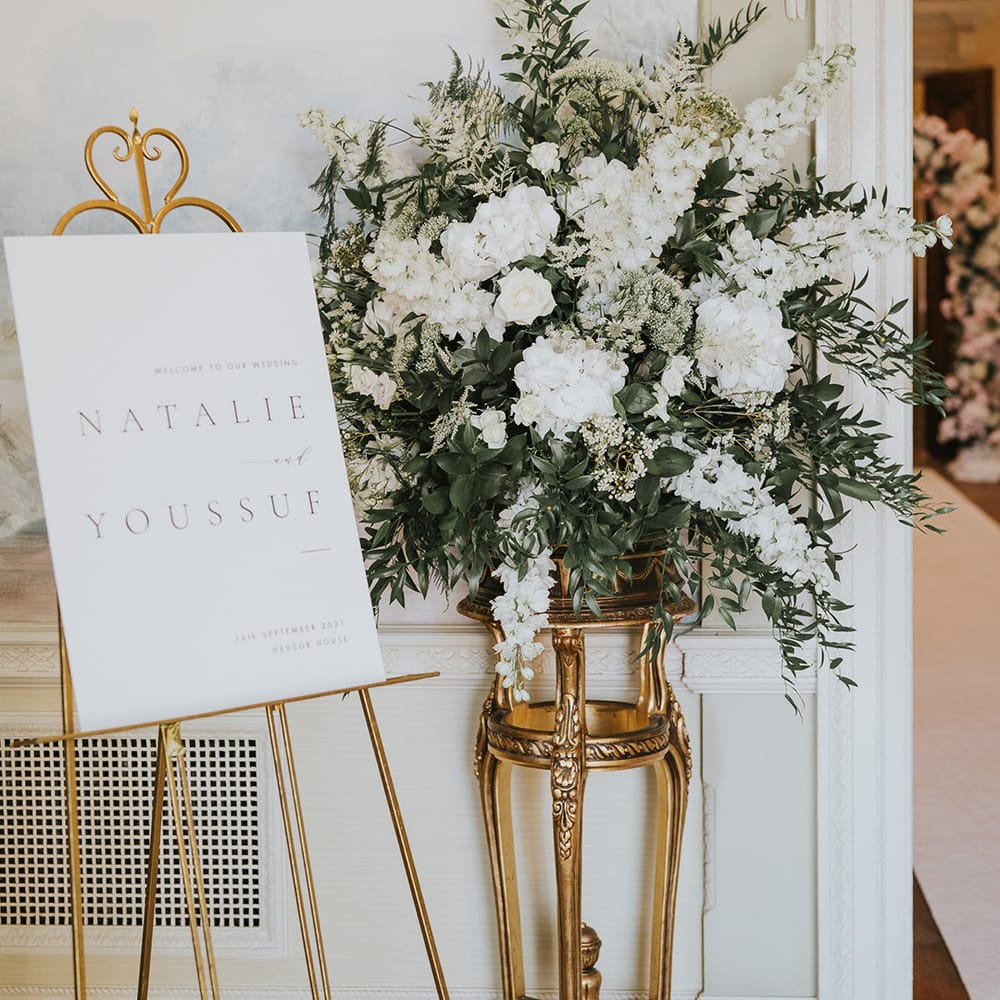 Classic black and white welcome wedding sign on gold easel with white flowers including stock for traditional country house wedding 