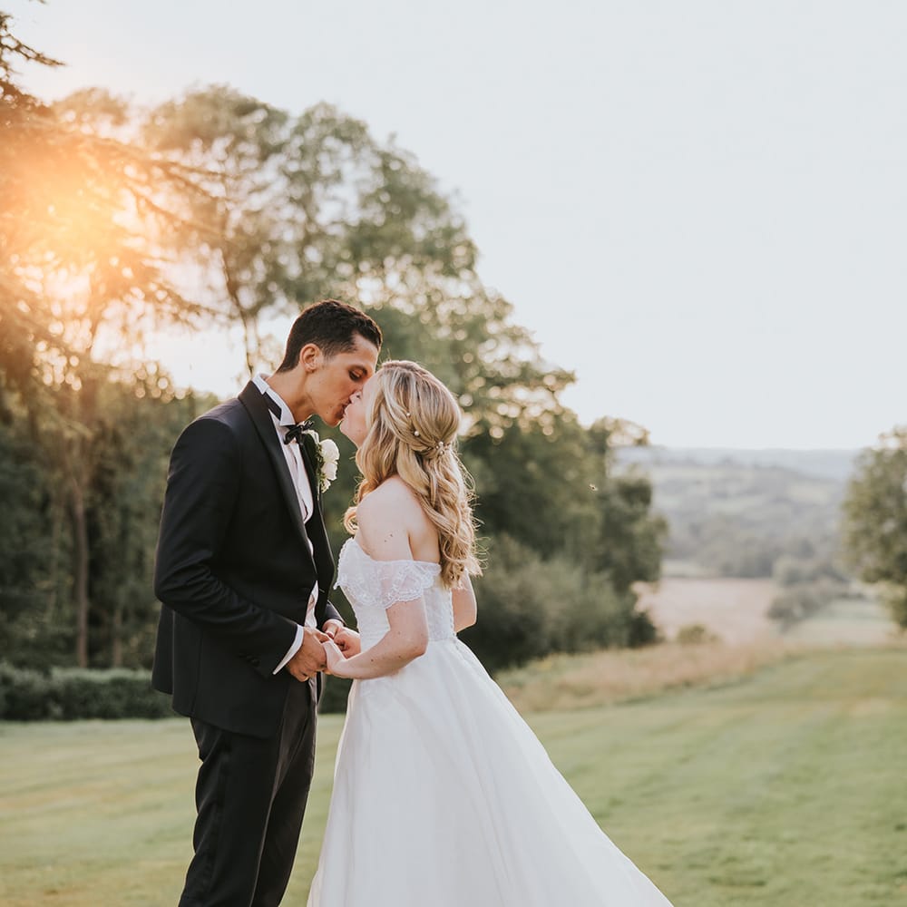 Bride and groom kiss overlooking the countryside around Hedsor House