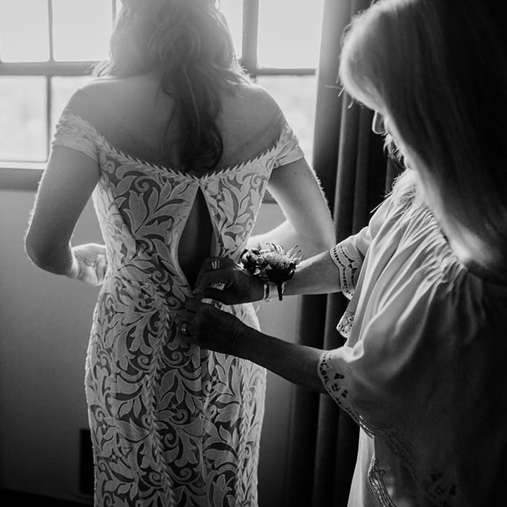 Mother of the bride helps zip the bride into her fitted lace wedding dress 