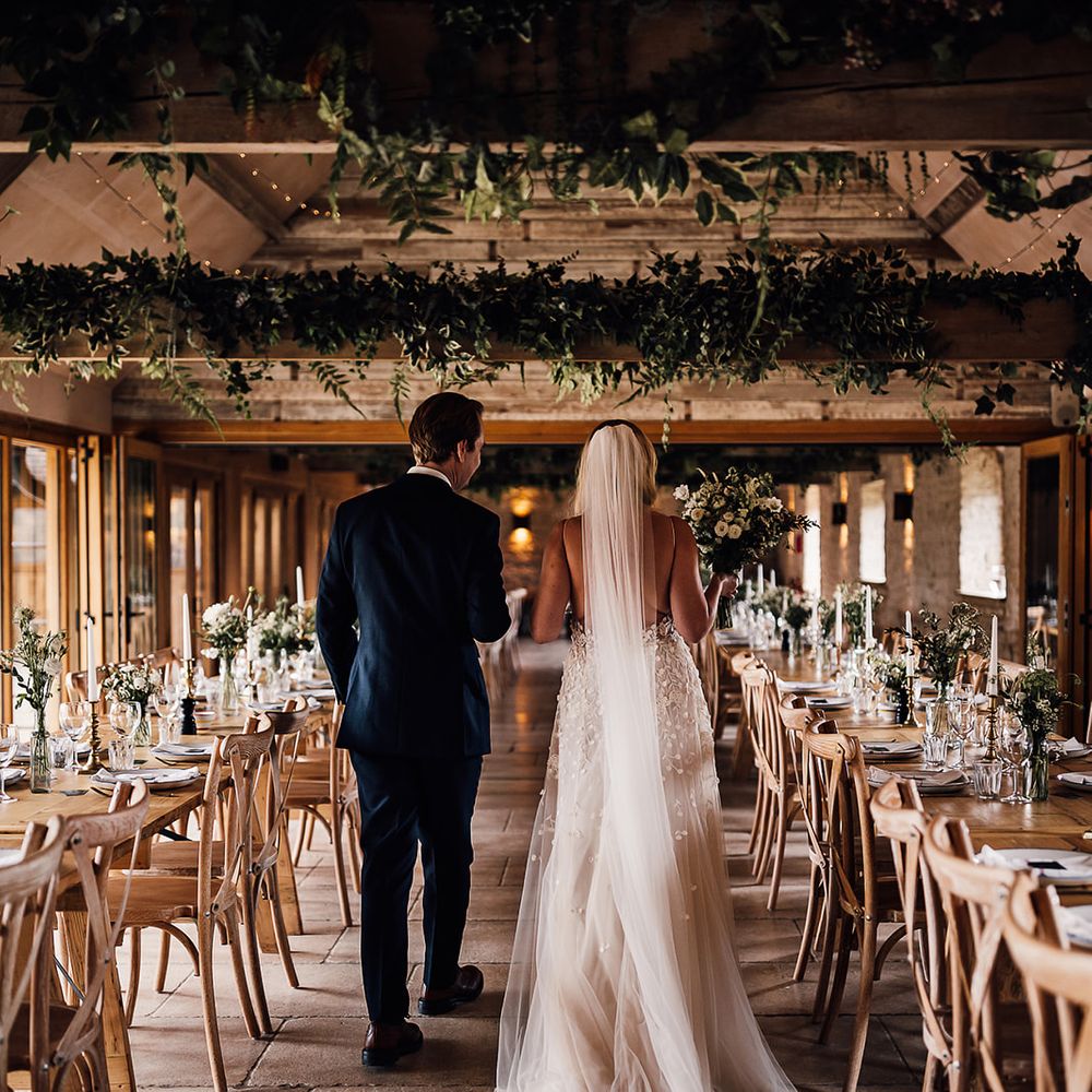 Bride and groom walk into Old Gore Barn for their wedding reception decorated in a classic style with a white and green tablescape 