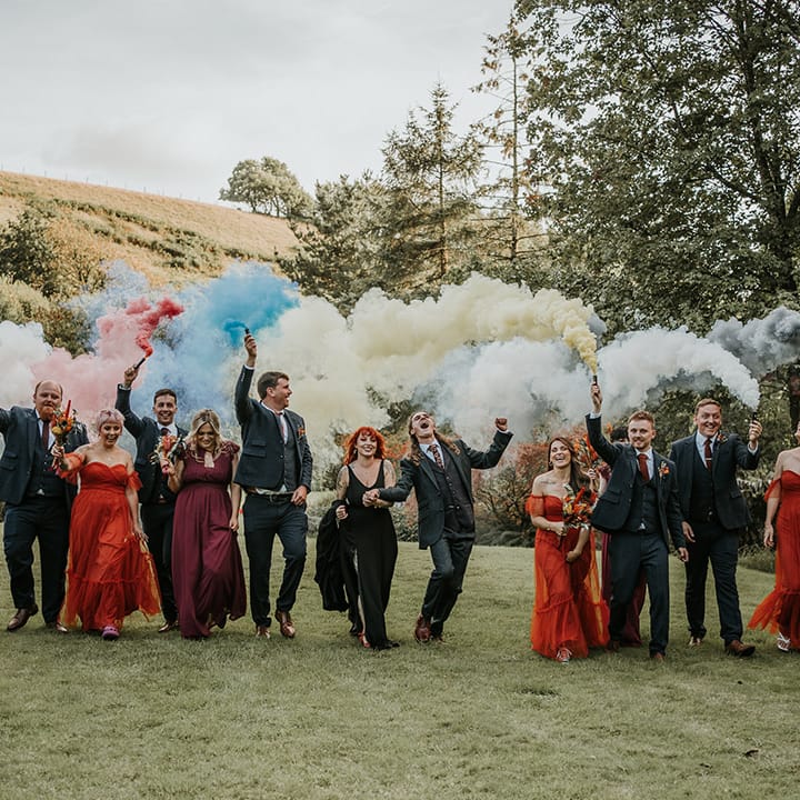 Wedding party in dark and burnt orange wedding outfits doing colourful smoke bomb photoshoot at Devon wedding venue 