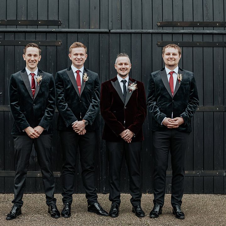 The groomsmen are wearing black velvet suit jackets with the groom in a burgundy velvet suit jacket 