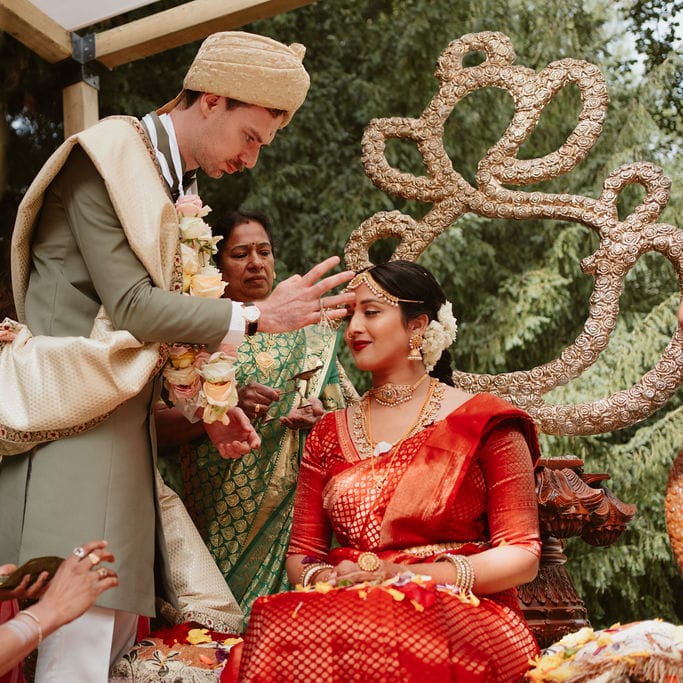 South asian bride in a red lehenga having paste put on her head during the Hindu wedding ceremony 