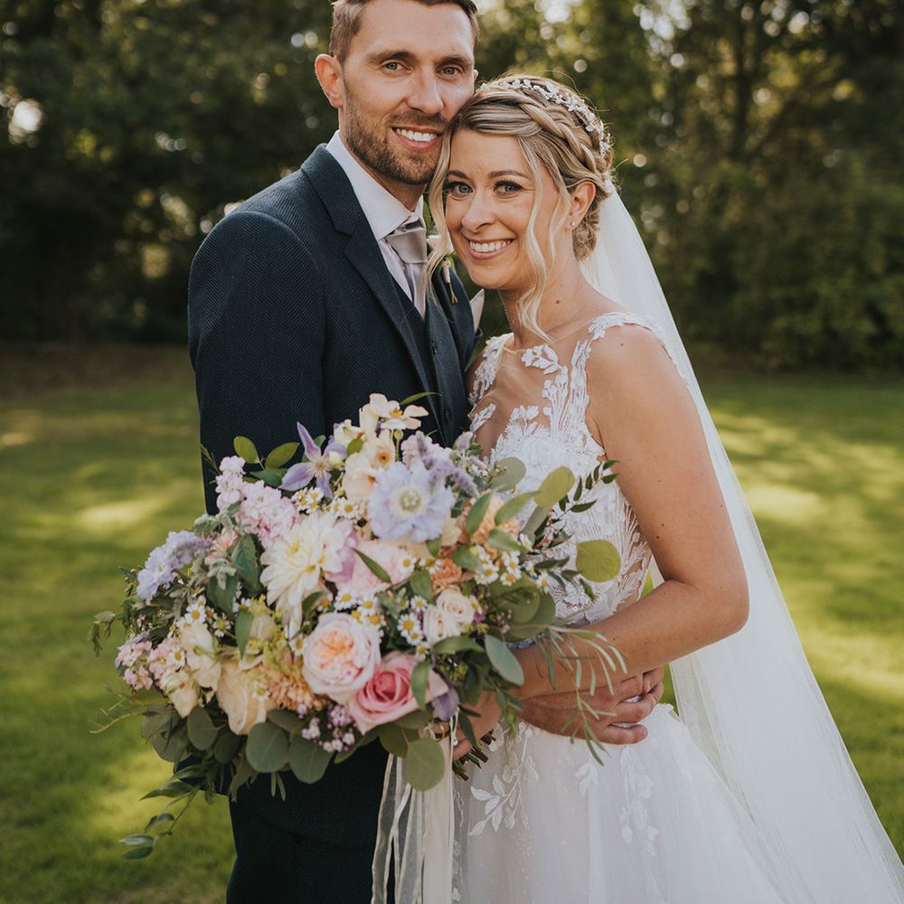 Bride in illusion lace wedding dress holding pretty pastel wedding bouquet with the groom in a dark suit for the Dove Barn in Suffolk wedding 