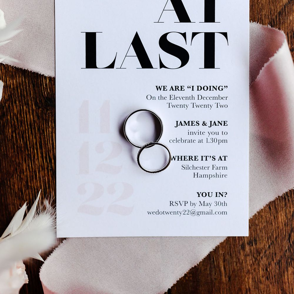 Black and white wedding invitation with the bride and groom's wedding rings with pink ribbon 
