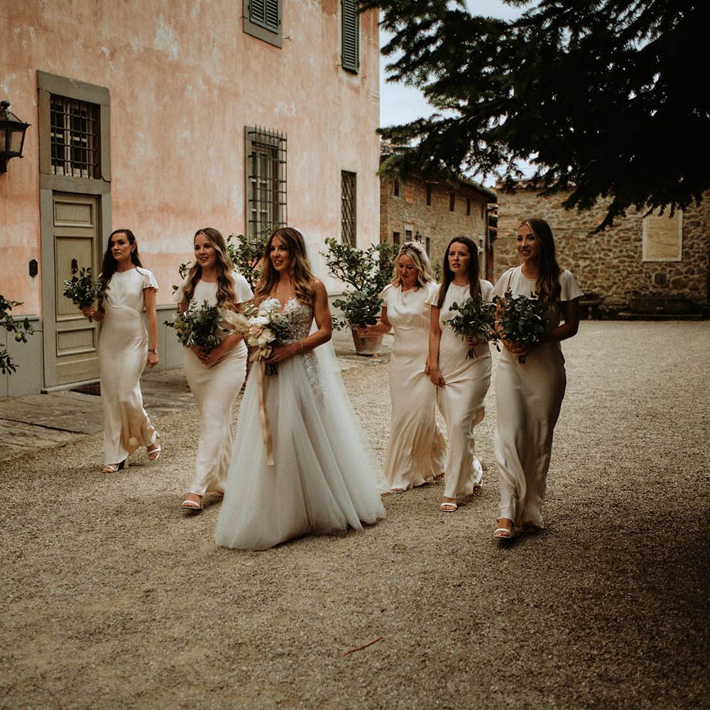 Bride in embroidered tulle wedding dress walking with bridesmaids in off white satin bridesmaids dresses at italian wedding villa holding eucalyptus bouquets