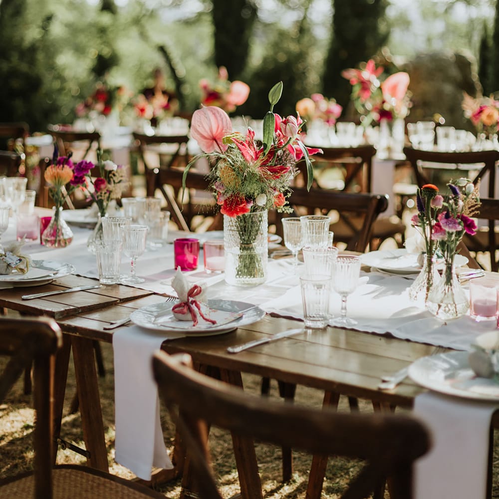 Rustic wooden tables with white and bright pink tablescape featuring vases of peonies, anthuriums, and bright pink flowers at woodland wedding in Italy