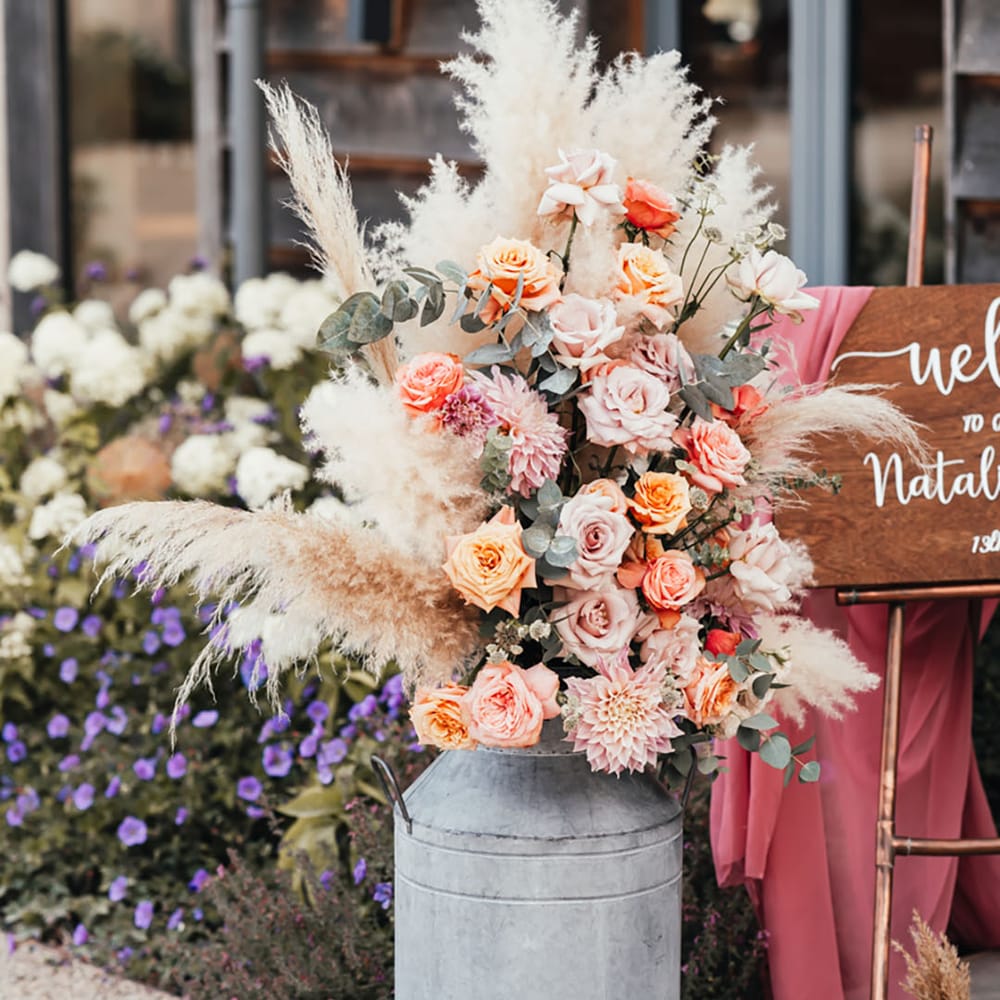 Vintage milk churn full of pink and orange roses with cafe au lait dahlias with pampas grass decor 